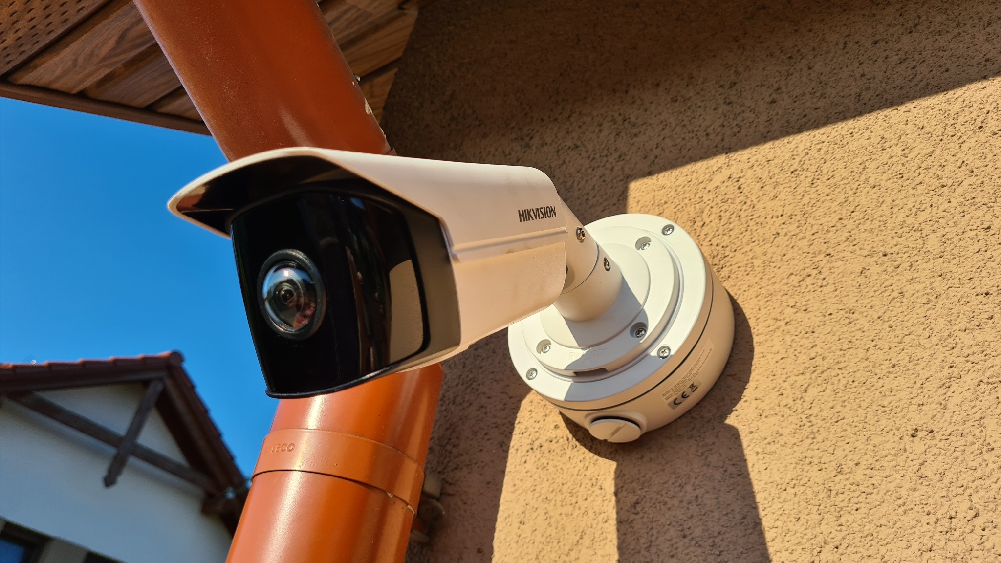 Kamera monitoringu Hikvision zamontowana na elewacji budynku, obok rury spustowej w słoneczny dzień.