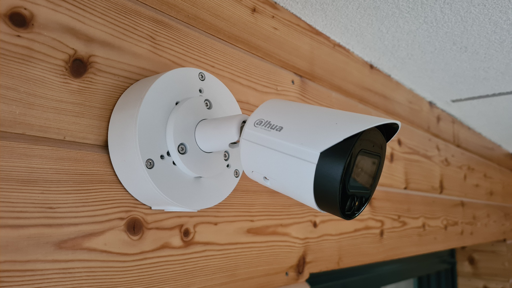 Biała kamera marki Dahua zamontowana na drewnianej ścianie, widoczne śruby mocujące i logo producenta.