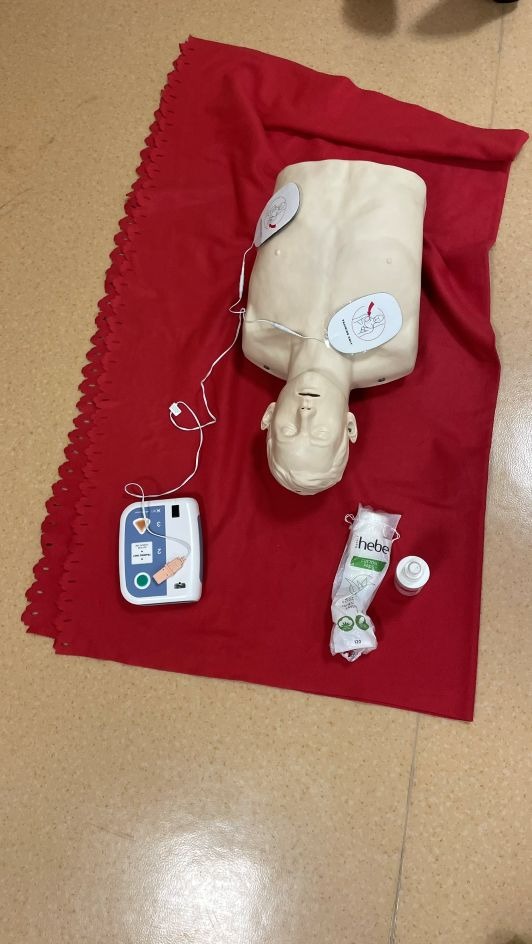 Manekin do resuscytacji z elektrodami, defibrylator, waciki na czerwonym tle. Sprzęt do kursu pierwszej pomocy, widok z góry.