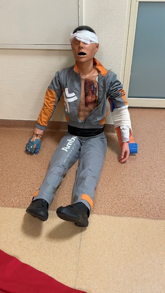 Manekin z ranami i bandażami, używany podczas kursu pierwszej pomocy. Widoczne realistyczne obrażenia i elementy ubioru manekina.