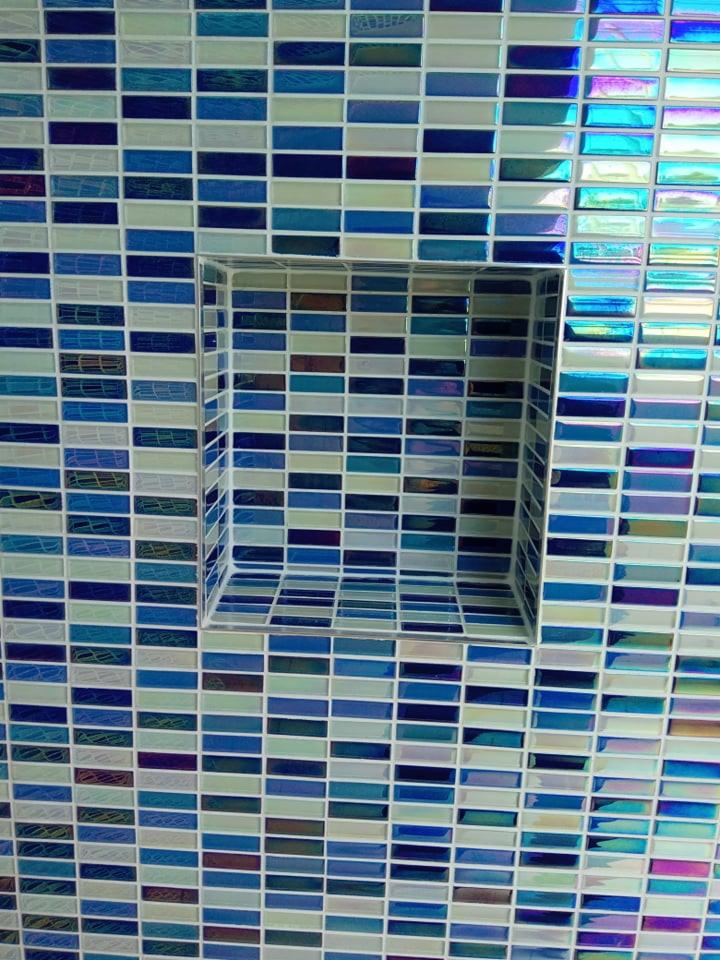 Ściana wyłożona mozaiką z podłużnych, szklanych płytek w odcieniach błękitu i turkusu, z wnęką wykończoną tym samym materiałem.