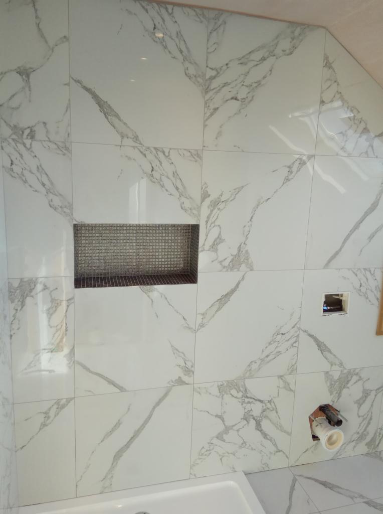 Ściana wyłożona białymi płytkami imitującymi marmur z wnęką wykończoną mozaiką w łazience w Rzeszowie, widoczny fragment instalacji hydraulicznej.