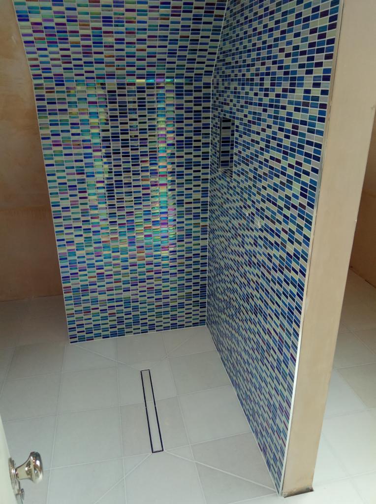 Kabina prysznicowa wykończona mozaiką w odcieniach błękitu i fioletu, z odpływem liniowym w jasnej podłodze.