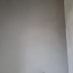 Gładka, szara ściana po nałożeniu tynku maszynowego, z widoczną rurką wystającą z dołu ściany.