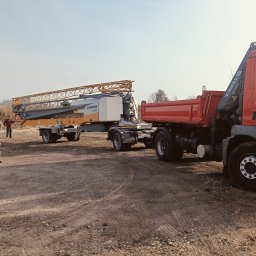 Z.U.B. Sklorz - Żuraw Liebherr LI-24 na naczepie, obok czerwona wywrotka Terex TGM 18.330, na placu budowy. Dwóch mężczyzn w tle. Słoneczny dzień.
