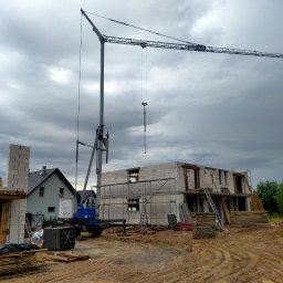 Z.U.B. Sklorz - Budowa domu z betonu komórkowego w trakcie wznoszenia, widoczny dźwig budowlany, rusztowania i ciężarówka z materiałami na tle pochmurnego nieba.