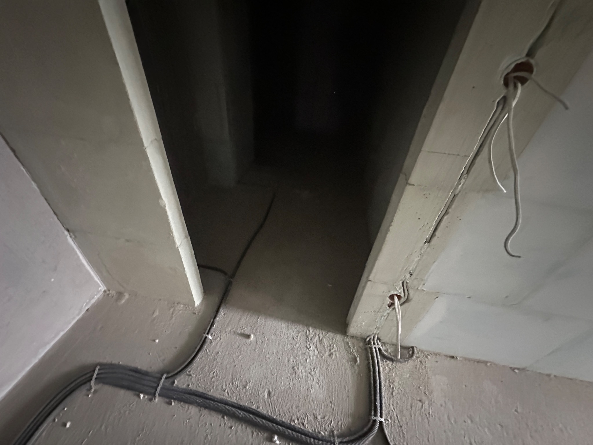 Szare kable elektryczne prowadzone wzdłuż sufitu z betonu architektonicznego, z widocznymi otworami na oświetlenie i wystającymi przewodami.