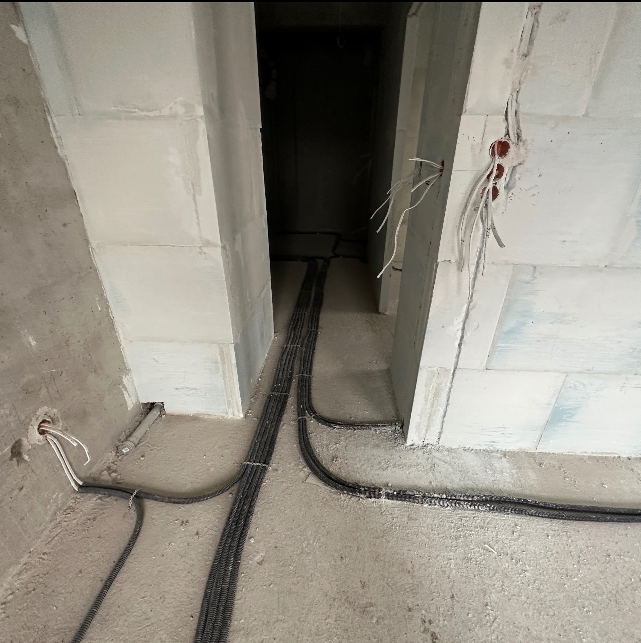 Wnętrze w trakcie prac wykończeniowych: kable elektryczne w peszlach ułożone na podłodze, wystające przewody ze ścian z betonu komórkowego.