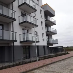 Nowoczesny budynek mieszkalny z balkonami i chodnikiem z kostki brukowej, widok z poziomu chodnika w pochmurny dzień.