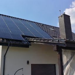 Dobry Klimat - Panele fotowoltaiczne na dachu domu jednorodzinnego z ciemną dachówką, widoczne anteny satelitarne i drabina oparta o ścianę.