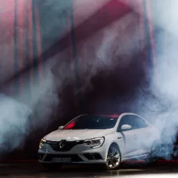 Biały samochód marki Renault w studiu, otoczony dymem, z widocznymi reflektorami i czerwonymi akcentami świetlnymi w tle.