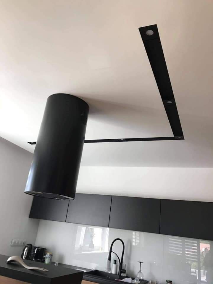 Nowoczesna kuchnia z czarną, cylindryczną wyspą kuchenną i minimalistycznym oświetleniem sufitowym w kształcie litery L z wbudowanymi punktami świetlnymi.