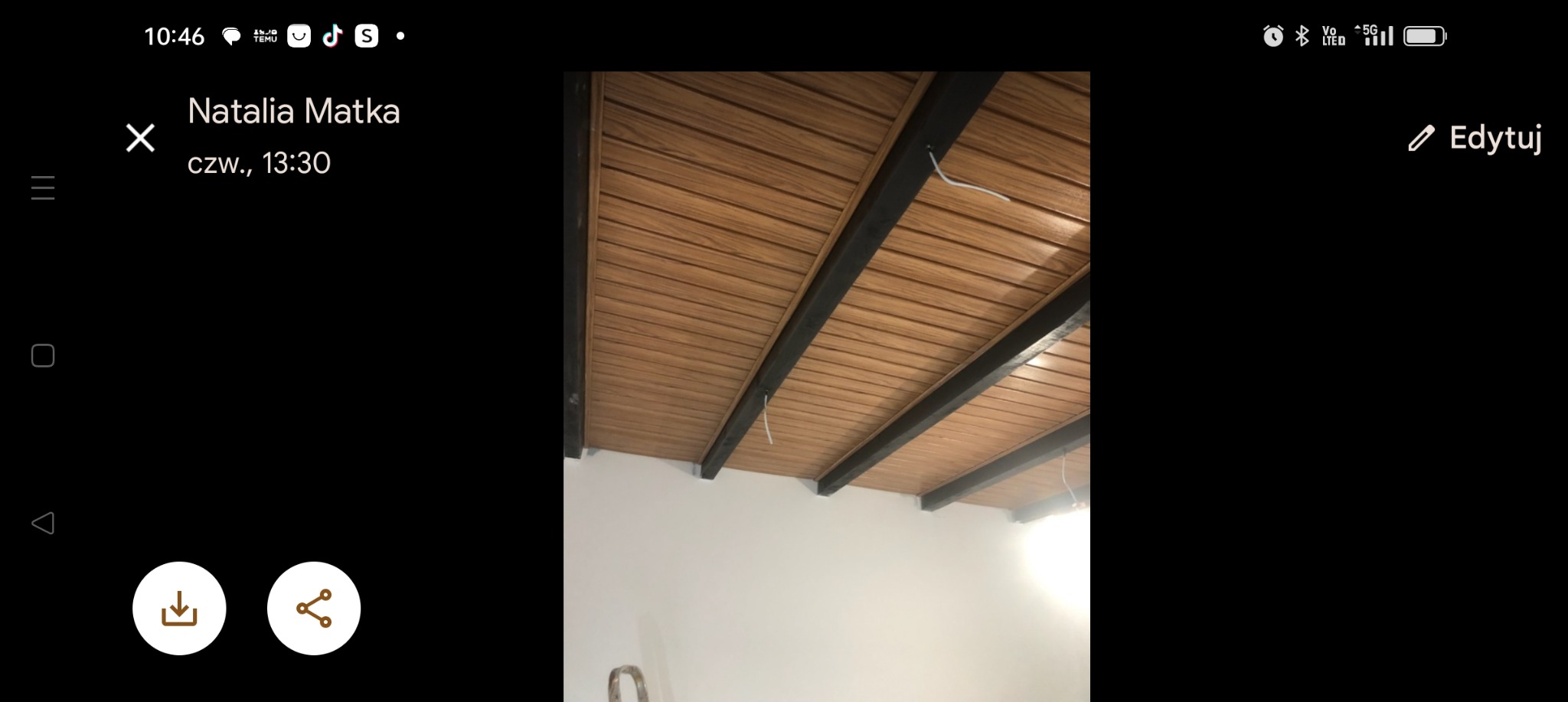 Drewnopodobna boazeria na suficie z czarnymi belkami konstrukcyjnymi, widok z dołu na białą ścianę.