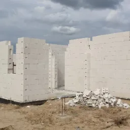 Wznoszone ściany parteru domu z białych bloczków betonu komórkowego, widoczne zbrojenia pionowe, na pierwszym planie sterta gruzu z tych samych bloczków, pochmurne niebo.