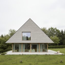 Moduu Magdalena Rosowska - Nowoczesny dom o trójkątnym kształcie z szarą elewacją i dużymi oknami, otoczony zielenią. Na tarasie leżak. Minimalistyczny design i naturalne otoczenie.