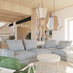 Moduu Magdalena Rosowska - Jasne, przestronne wnętrze domu z drewnianymi elementami, szarą sofą modułową i okrągłym stolikiem kawowym. Widoczne schody i regał z książkami. Dwie lampy wiszące.