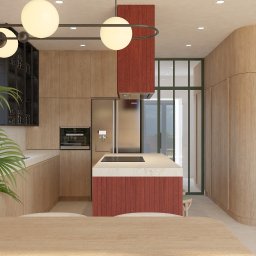 Moduu Magdalena Rosowska - Nowoczesna kuchnia z drewnianymi szafkami, wyspą z czerwonym akcentem i okrągłymi lampami. Roślina w rogu dodaje świeżości. Widok na przeszklone drzwi.