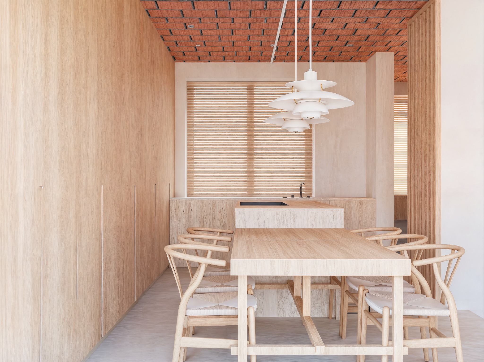 Jasne drewno dominuje w minimalistycznej jadalni z ceglanym sufitem. Stół z krzesłami, zabudowa kuchenna i żaluzje tworzą spójną, ciepłą przestrzeń.
