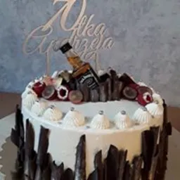 Tort urodzinowy z białym kremem, dekorowany czekoladowymi wi&oacute;rkami, owocami i miniaturową butelką Jack Daniel's, z topperem z imieniem na 70 urodziny.