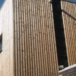 Nowoczesny dom z elewacją z pionowych drewnianych desek, z fragmentem widocznej instalacji odprowadzającej wodę deszczową i małym oknem.