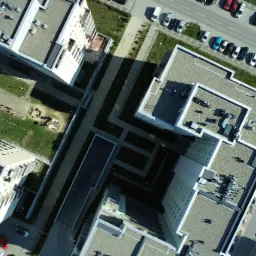 Zdjęcie z lotu ptaka przedstawia kompleks budynków mieszkalnych z wewnętrznym dziedzińcem, placem zabaw i parkingiem.