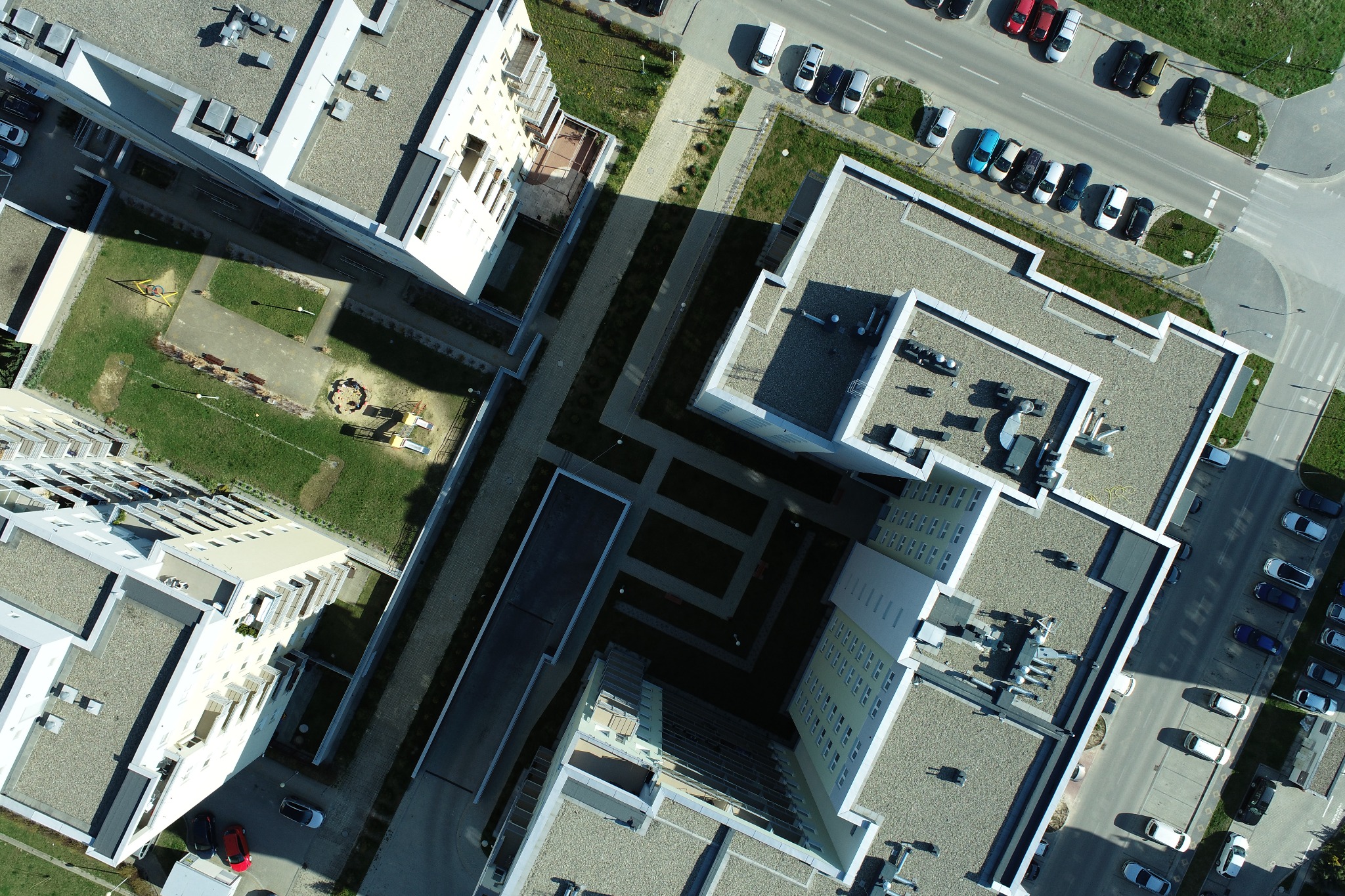 Zdjęcie z lotu ptaka przedstawia kompleks budynków mieszkalnych z wewnętrznym dziedzińcem, placem zabaw i parkingiem.