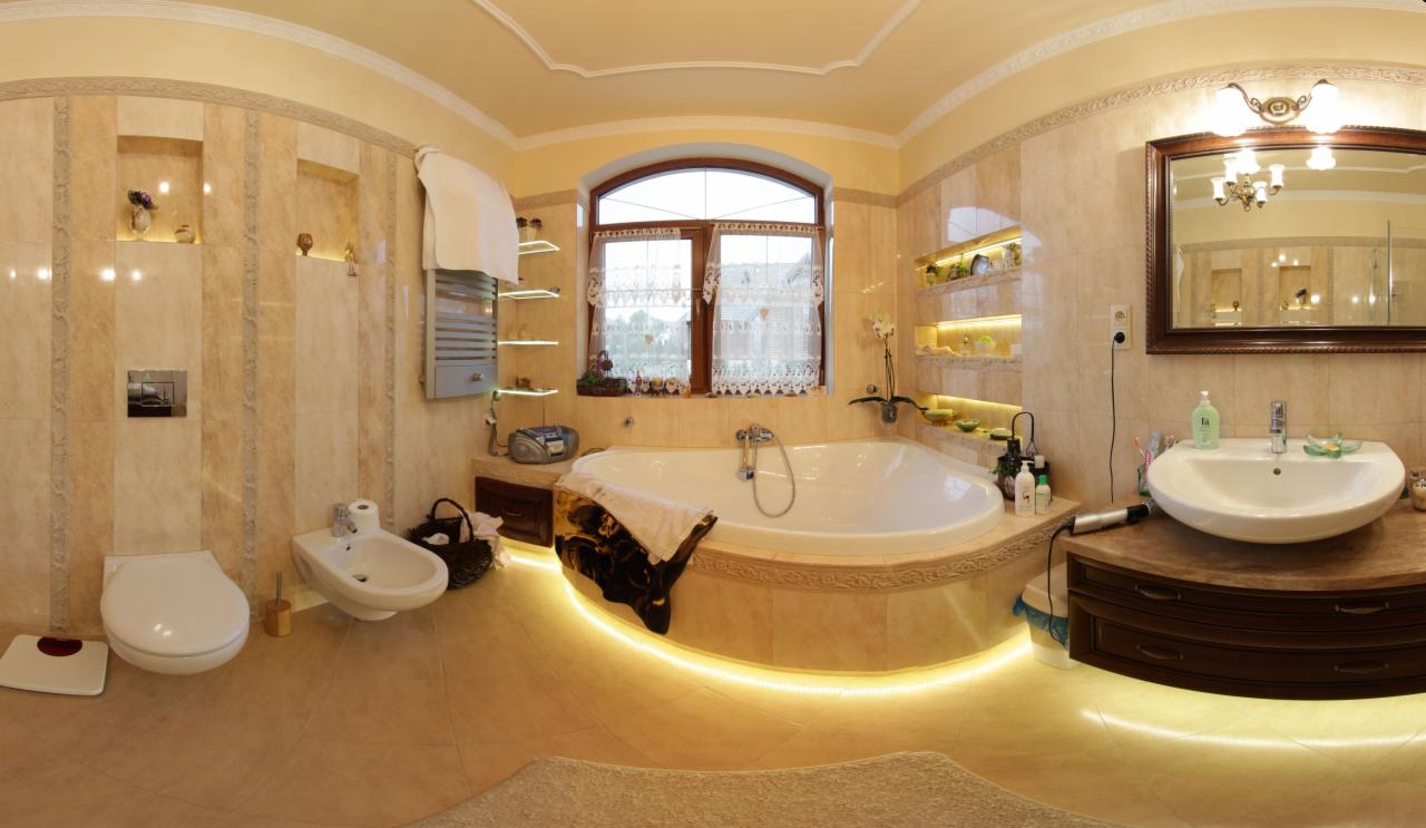 Przestronna łazienka z wanną narożną pod oknem, beżowymi płytkami, podświetleniem LED, umywalką nablatową i toaletą z bidetem, widziana z perspektywy panoramicznej.