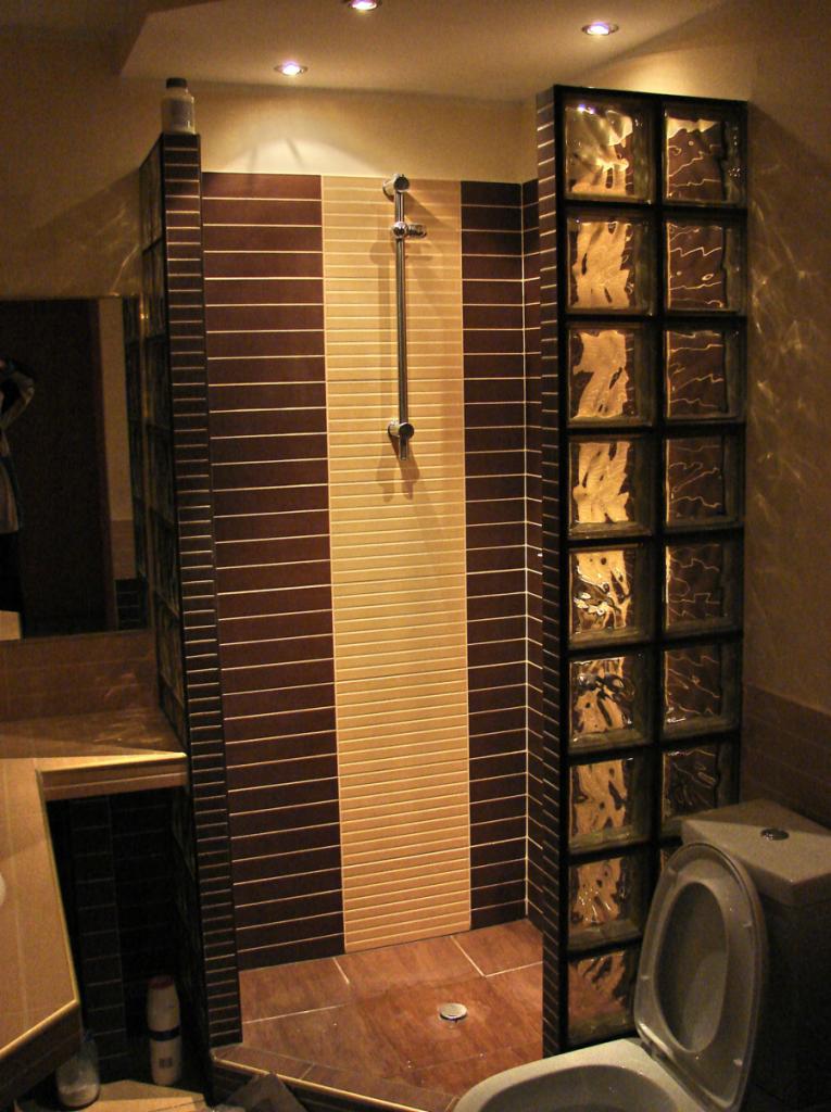 Kabina prysznicowa z elementami szklanymi, wykończona brązowo-beżowymi płytkami, widoczna toaleta.