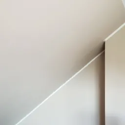 Pomalowane na beżowo poddasze ze skosem, widoczna biała listwa wykończeniowa i fragment drabiny malarskiej.