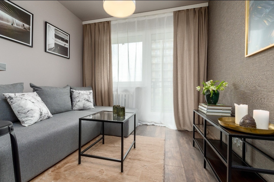 Jasne, nowocześnie urządzone wnętrze salonu w Zabrzu z szarym narożnikiem, stolikiem kawowym i dekoracjami na komodzie.