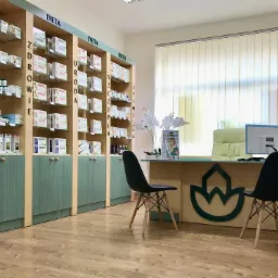 Gabinet z regałami pełnymi suplementów diety, biurkiem z komputerem i dwoma krzesłami, jasne wnętrze z drewnianą podłogą.