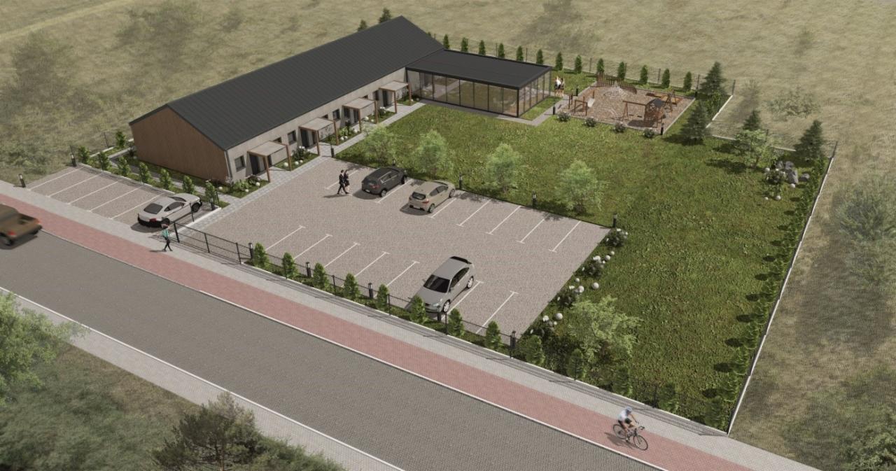 Wizualizacja architektoniczna parterowego budynku z parkingiem, placem zabaw i zielenią, widok z lotu ptaka.
