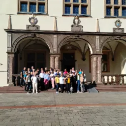 Grupa turystów pozuje na schodach zabytkowego budynku z łukami, widoczny podjazd dla wózków inwalidzkich.