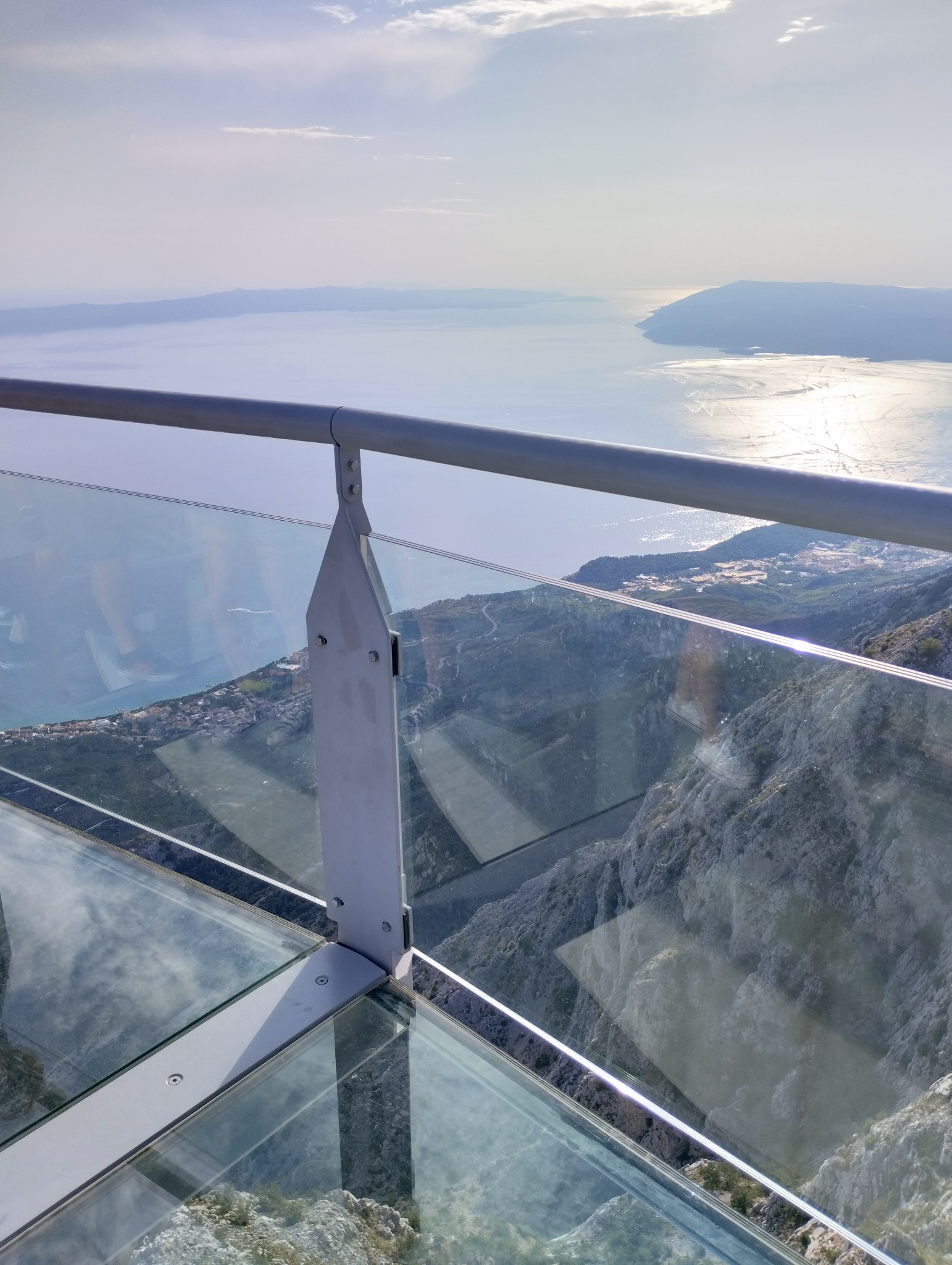 Szklany taras widokowy na górze z metalową barierką, widok na morze i góry w oddali.