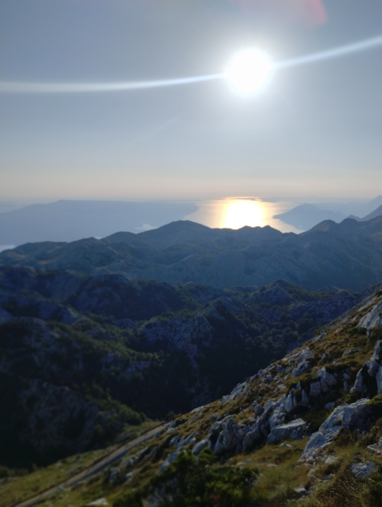 Widok z góry na górzysty krajobraz z morzem w tle, oświetlony silnym słońcem.