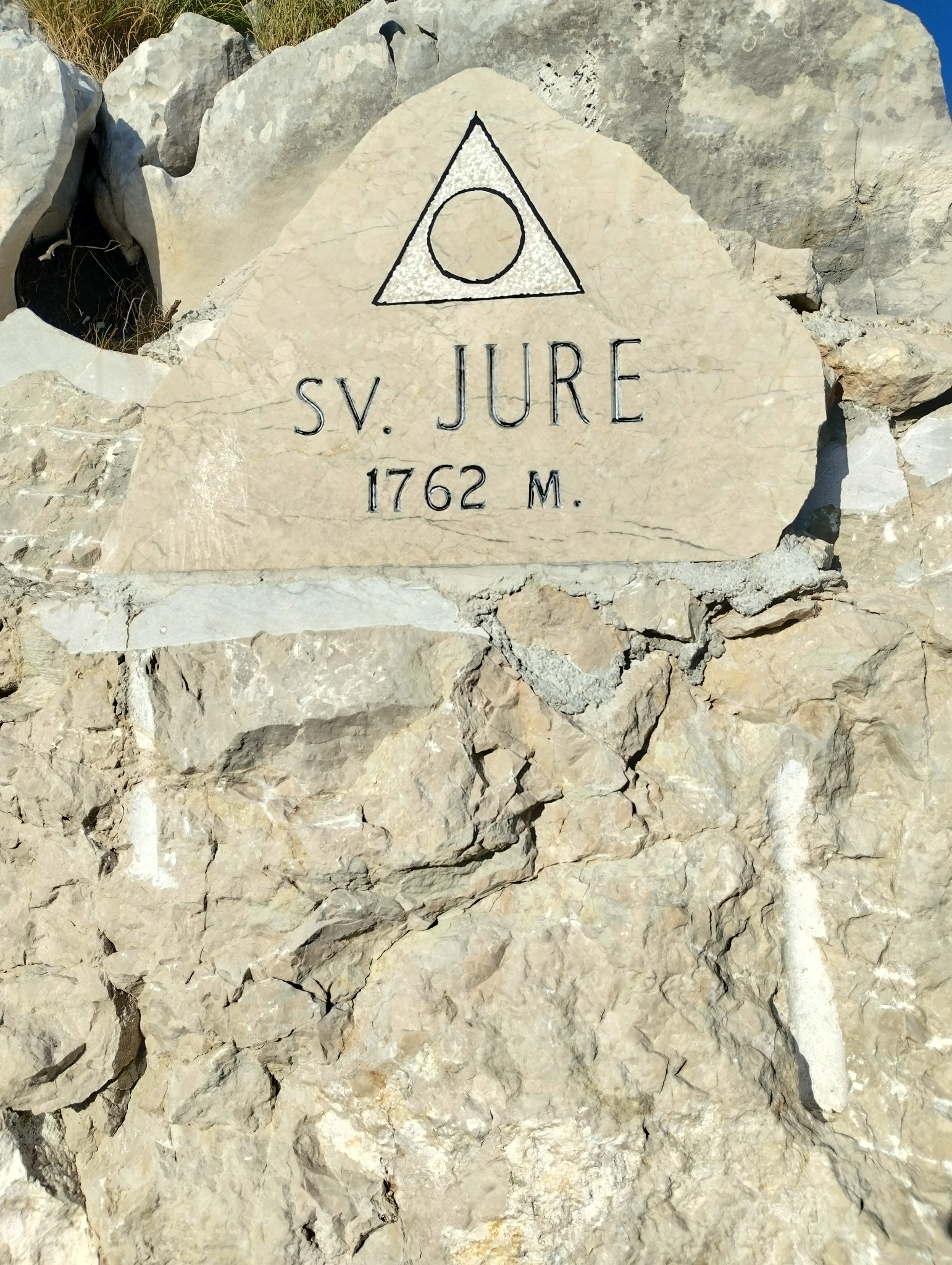 Kamienna tablica z symbolem trójkąta z okręgiem i napisem SV. JURE 1762 M. umieszczona na skalnej ścianie.
