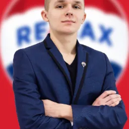 Portret młodego mężczyzny w niebieskiej marynarce z przypinką logo agencji nieruchomości na tle rozmytego logo firmy.