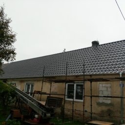 Jar-Bud - Dom z nowym, ciemnoszarym dachem z dachówki ceramicznej, widoczny z poziomu gruntu, z rusztowaniem i podnośnikiem dekarskim. Częściowo otynkowana elewacja.