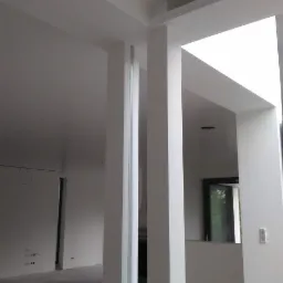 Wnętrze w trakcie wykańczania, widoczne białe ściany, filary z wnęką i surowa podłoga, instalacja elektryczna widoczna na ścianie w tle.