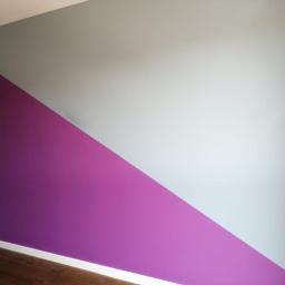Danpol - Ściana pomalowana w Lublinie na dwa kolory: fioletowy i szary, oddzielone ukośną linią, z widoczną listwą przypodłogową i fragmentem drewnianej podłogi.