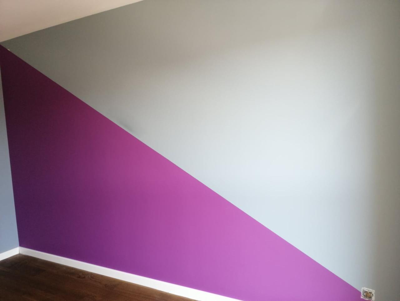 Ściana pomalowana w Lublinie na dwa kolory: fioletowy i szary, oddzielone ukośną linią, z widoczną listwą przypodłogową i fragmentem drewnianej podłogi.