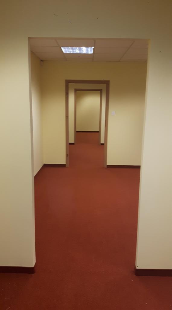 Korytarz biurowy z czerwoną posadzką i szeregiem drzwi bez klamek, widok perspektywiczny z niskiego kąta.