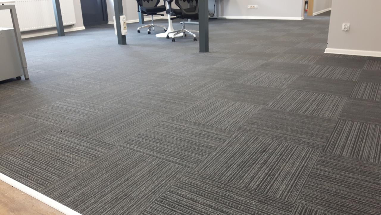 Biuro z szarą wykładziną dywanową w kwadraty, widoczne biurka i krzesła w tle.