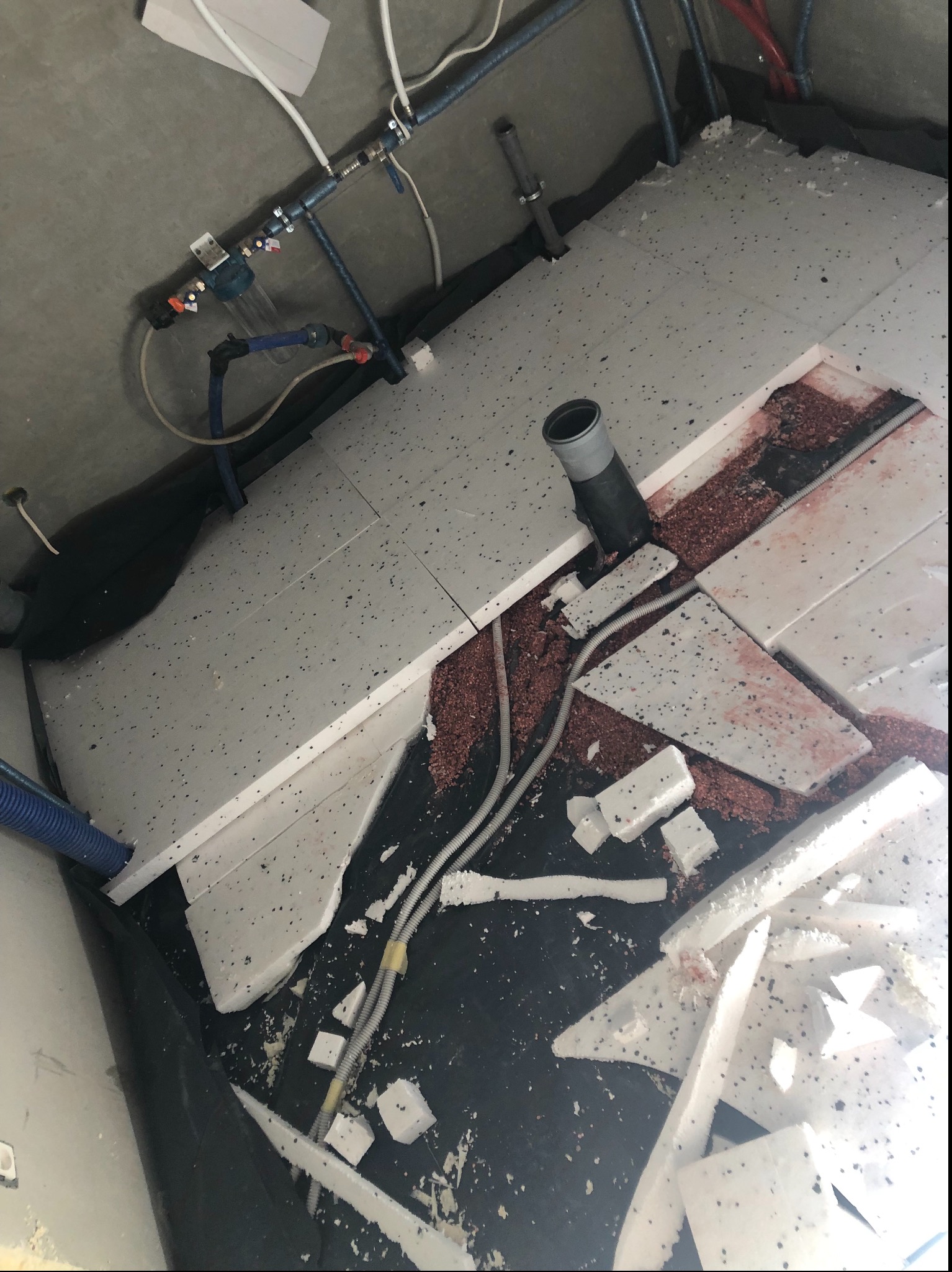 Przygotowanie podłoża pod wylewkę: styropian podłogowy z widocznymi rurami instalacji wodnej i kanalizacyjnej w surowym pomieszczeniu.