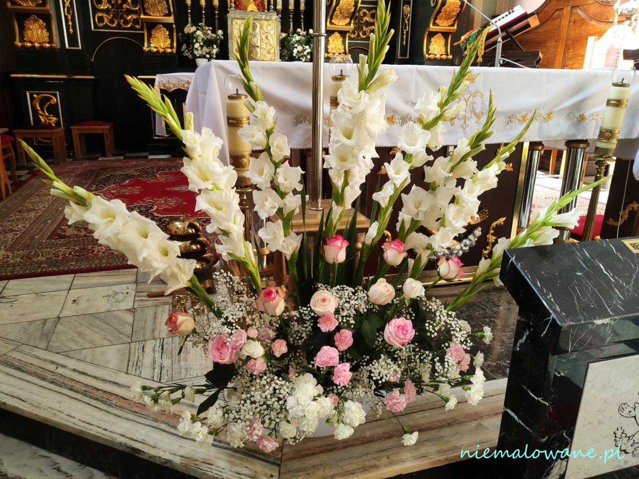 Dekoracja kwiatowa z białych mieczyków i różowych róż w kościele, widok z dołu na marmurową posadzkę.