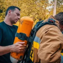 Instruktor demonstruje prawidłowe mocowanie butli tlenowej do uprzęży ratowniczej podczas szkolenia z zakresu bezpieczeństwa.