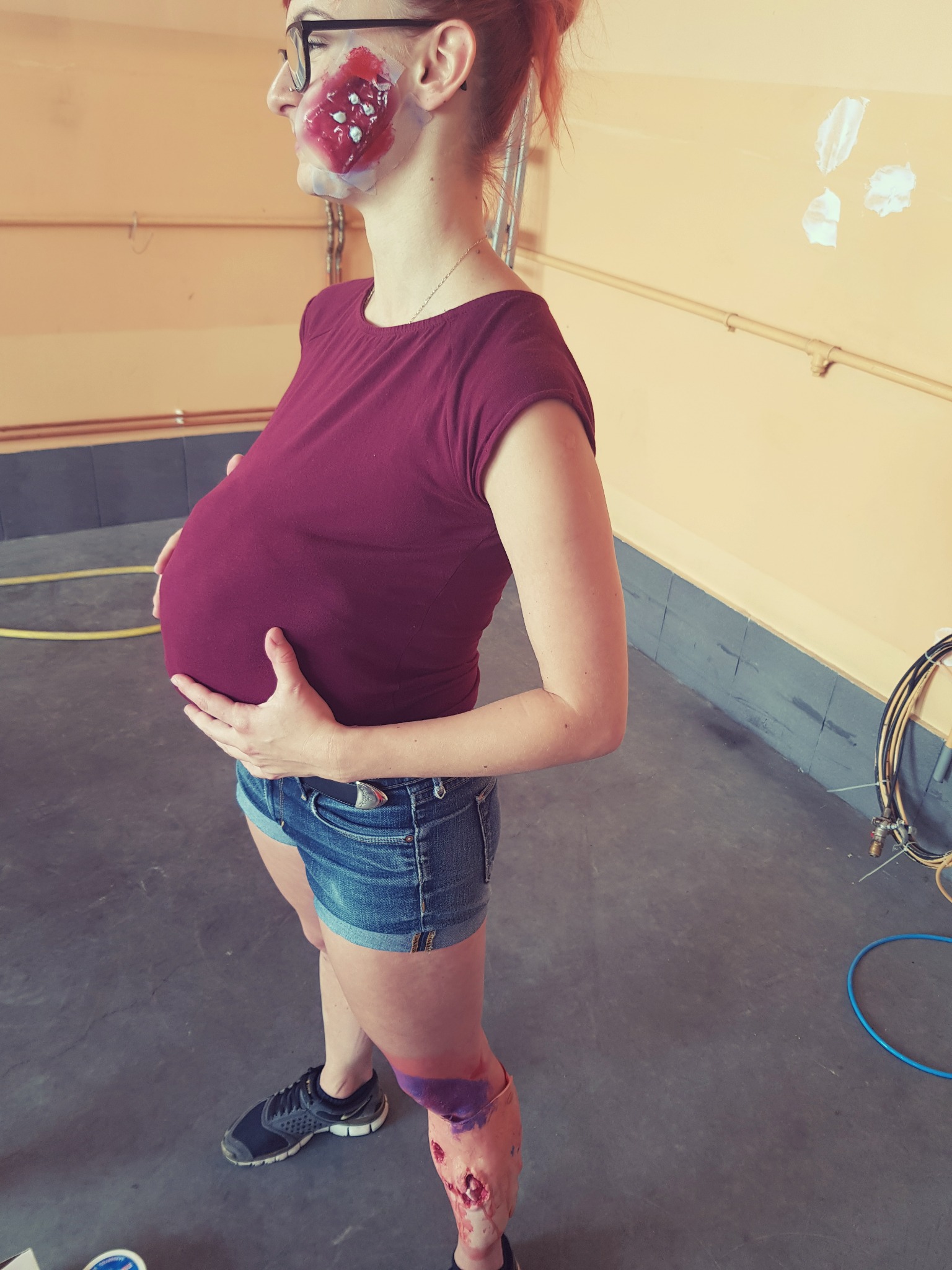 Osoba z realistycznym makijażem symulującym obrażenia na twarzy i nodze, prawdopodobnie podczas szkolenia z pierwszej pomocy.