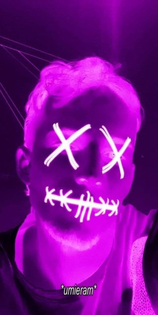 Portret osoby z neonowym makijażem w odcieniach fioletu, przedstawiającym znak 'X' na oczach i szwy na ustach, tworząc efektowny, artystyczny wygląd.