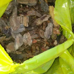 Worek z żółtej folii wypełniony kawałkami kory drzewnej o nieregularnych kształtach i brązowo-szarej barwie.