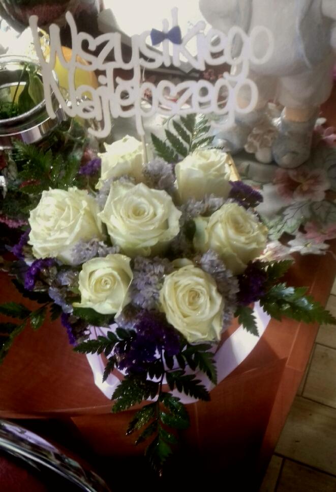 Kompozycja z kremowych róż i fioletowych kwiatów, z napisem 'Wszystkiego Najlepszego' na drewnianym topperze, umieszczona w białym koszyczku.